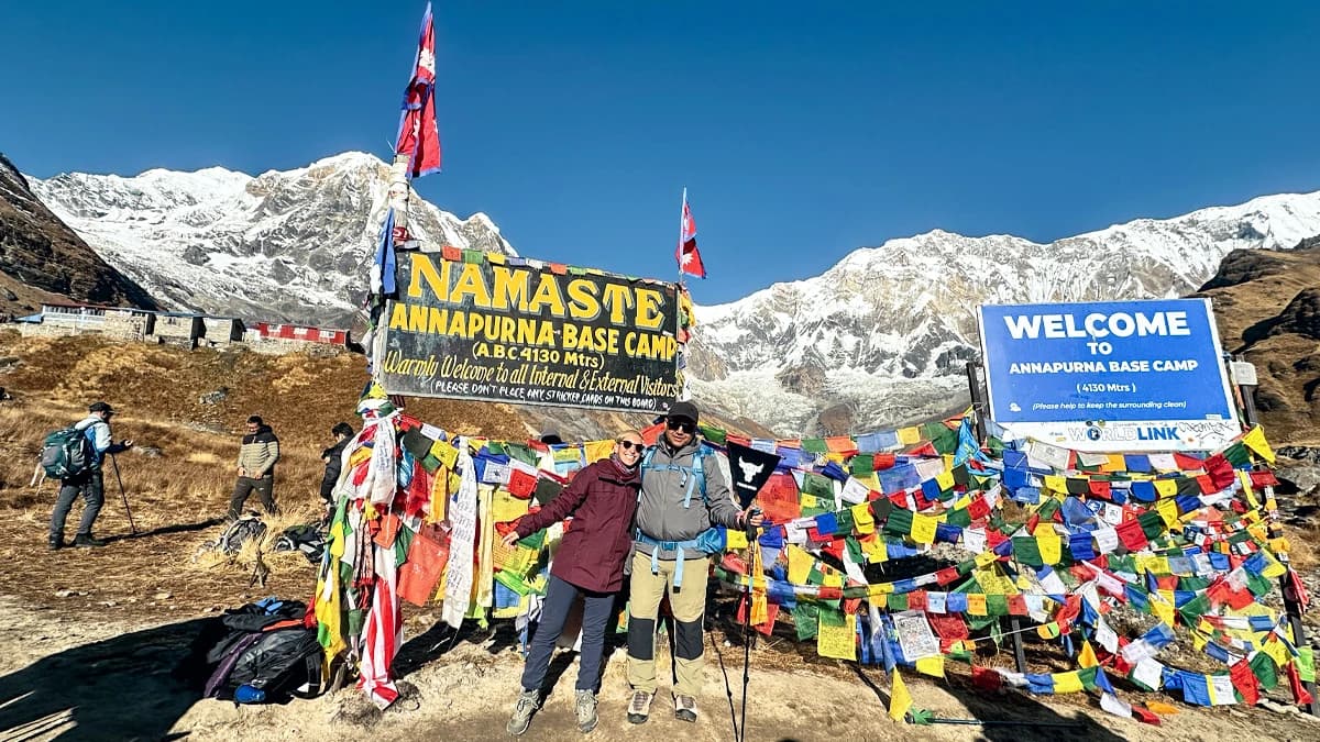 Trekkers standing in front of the Annapurna Base Camp board with Annapurna South in the background